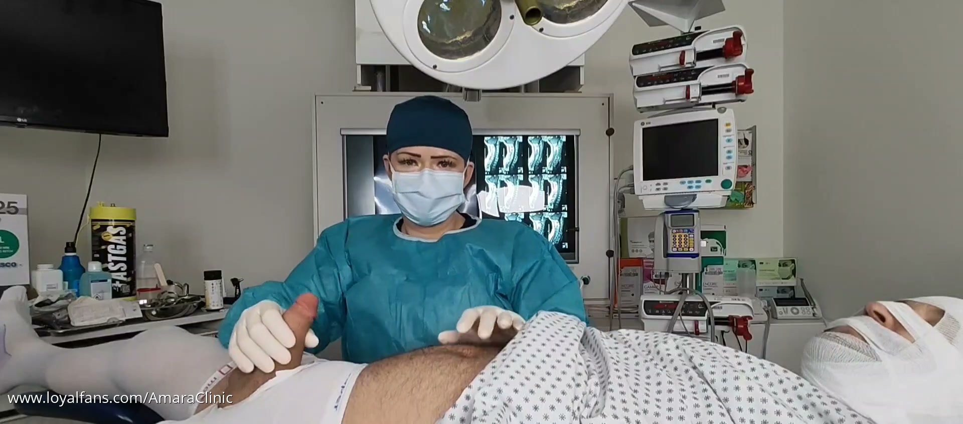 Mistress Katharina Amara urology clinic video: the Dominatrix holding a metal sounding rod and a tray of sterile instruments over her patient during a clinical examination in her klinik BDSM sounding room