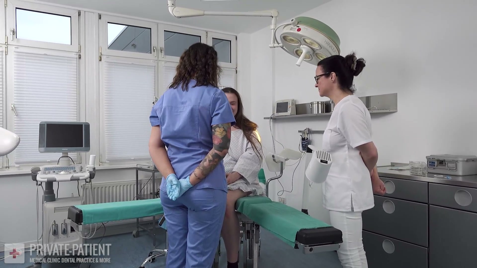 Dr. Eve and Dr. Lana van Orten in white coats and surgical gloves welcoming a new private patient in the free Dr. Eve Private Patient first part medical BDSM femdom video from Amara Fetish Clinic Belgium