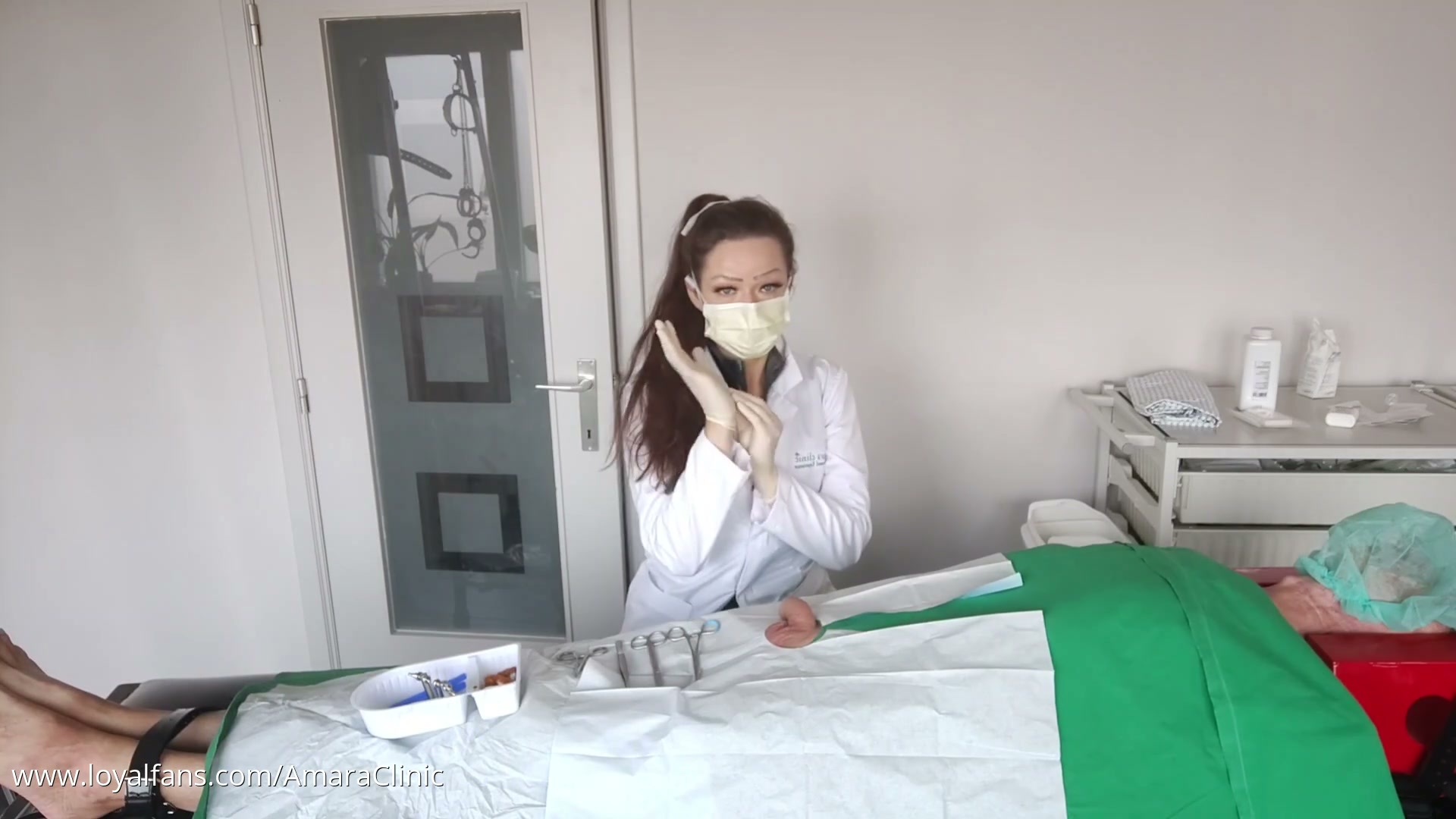 Mistress Katharina Amara in brown Ansell gloves suturing a urethral separator onto a patient cock in a free penile surgery medfet video